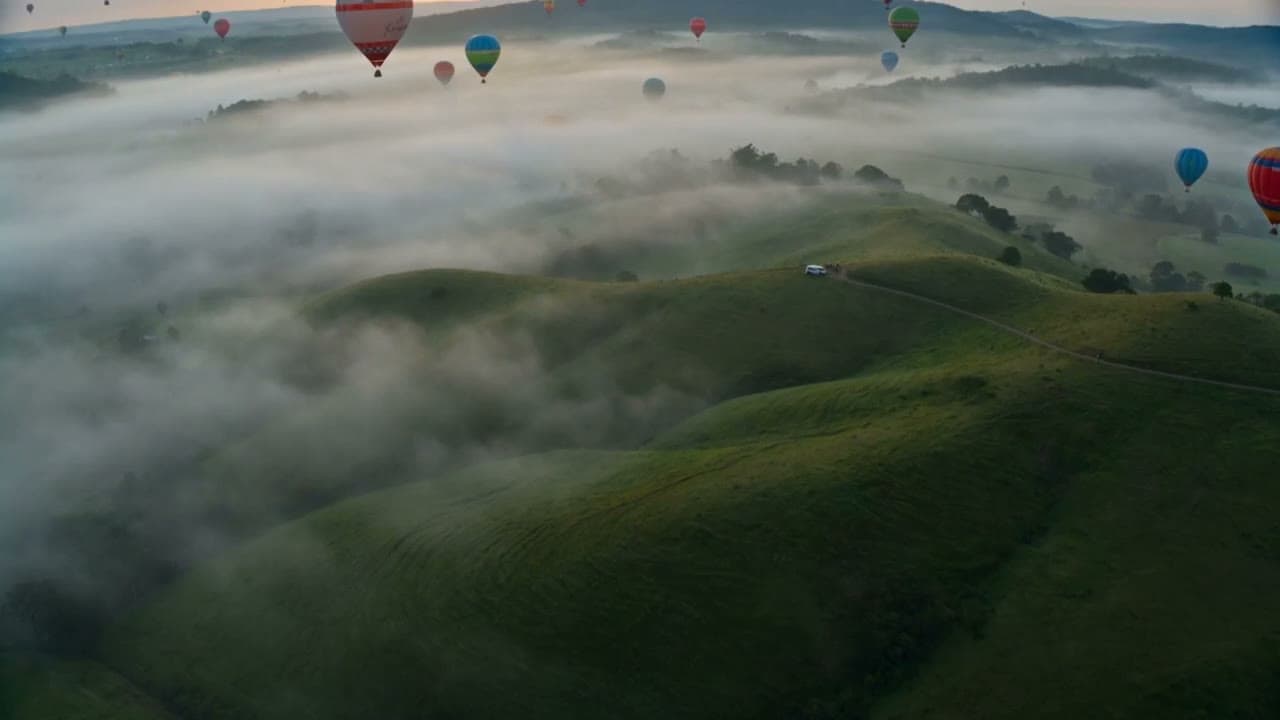 Hot air balloons over green hills and morning fog